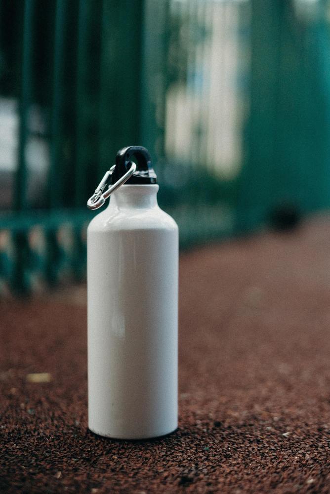 A white water bottle with a black lid sitting on the ground in dirt