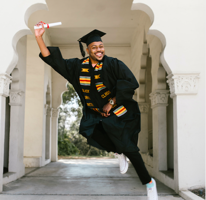 young man in graduation gown jumping and smiling