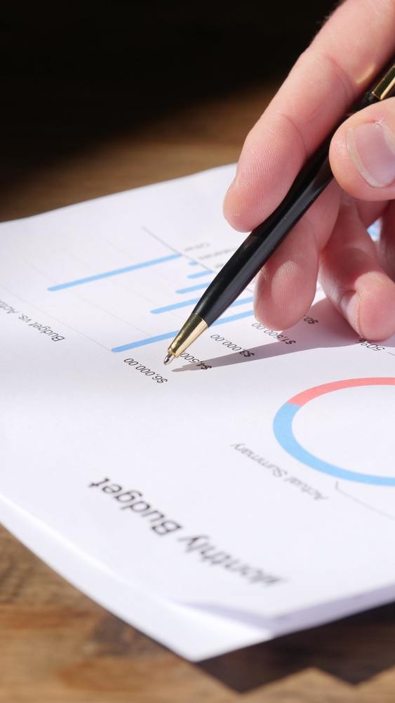 A hand holding a pen over a paper that says Monthly Budget
