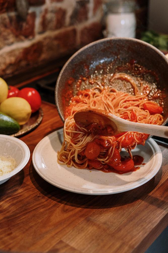 A skillet spooning out spaghetti onto a plate