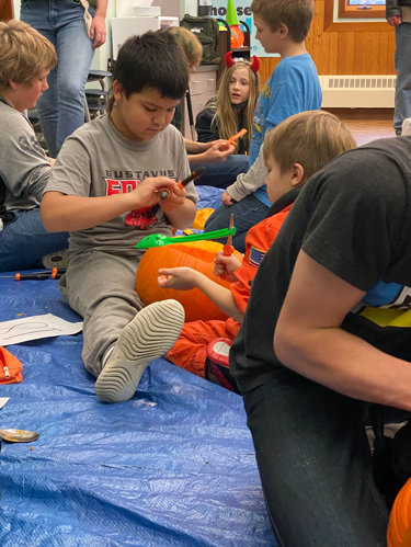 Kids sitting on a tarp with pumpkins and pumpkin carving tools