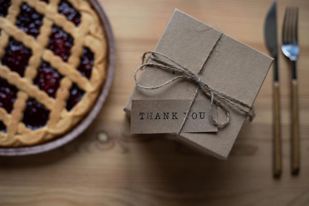A pie on a table with a small gift that says Thank You on the tag